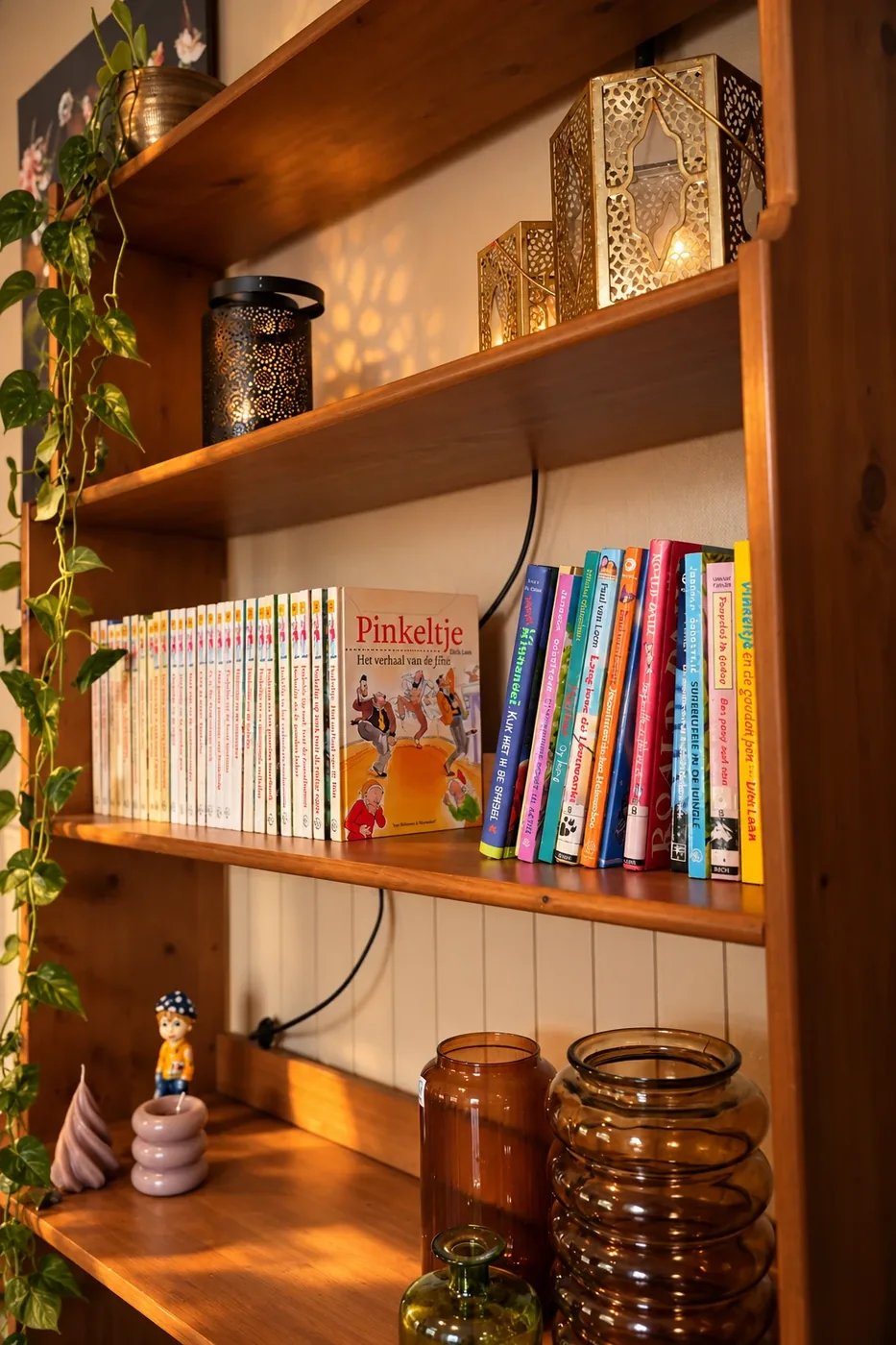 Een boekenkast met kinderboeken, kaarsen en een plant in de woonkamer